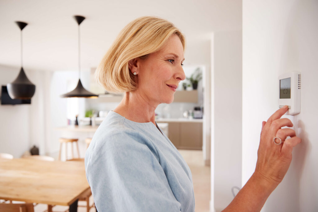 Woman Adjusting Central Heating Temperature At Home On Thermostat